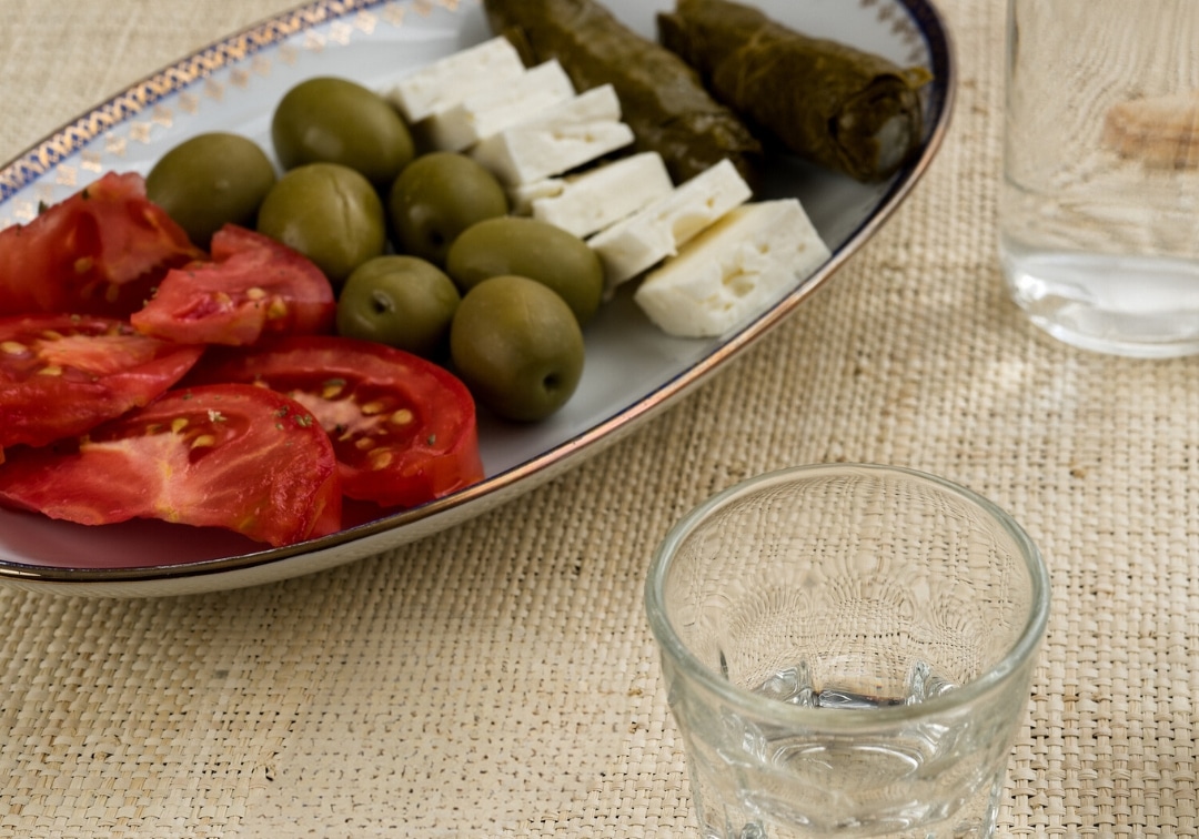 An image of greek mezze, feta cheese, sliced tomato, olives and stuffed vineleaves