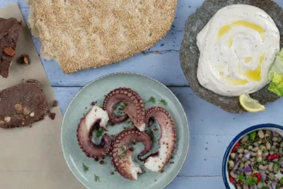 A complete traditional Greek Lenten meal featuring grilled octopus, black-eyed pea salad, taramasalata, lagana bread, and cocoa halva.